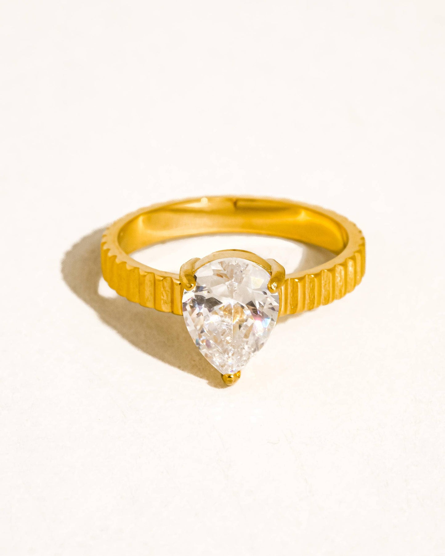 Close-up of the Vow Ring an 18K gold-plated stainless-steel statement ring featuring a pear-cut cubic zirconia, photographed on a soft neutral display.