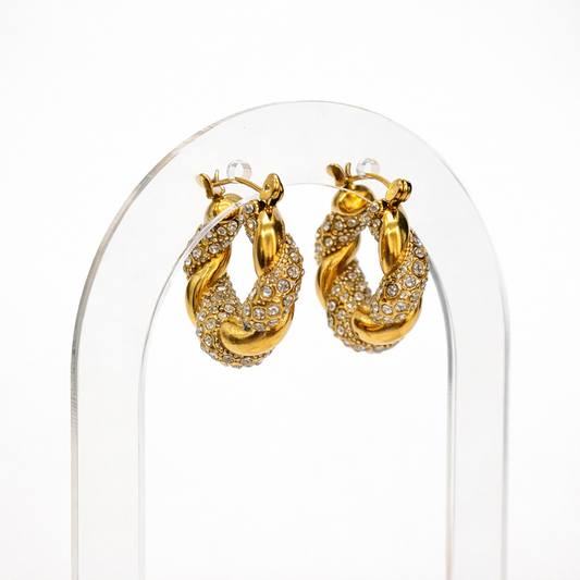 Gold twisted hoop earrings with clear zirconia stones on decorative tray by Atelier Épure — elegant, timeless, and refined.