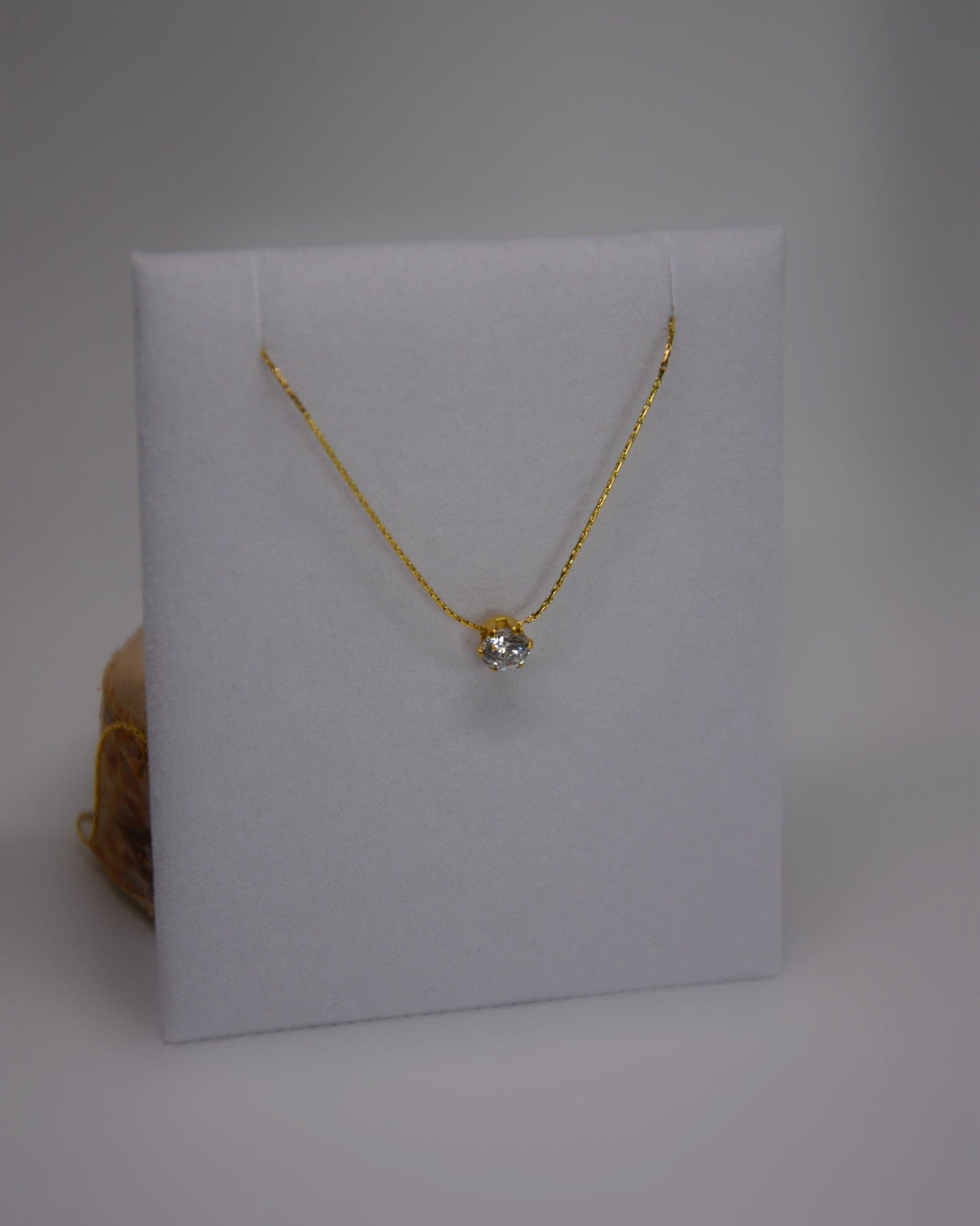 Close-up of the Serein Necklace, a dainty 18K gold-plated chain featuring a small round cubic zirconia pendant, photographed on a soft neutral display.