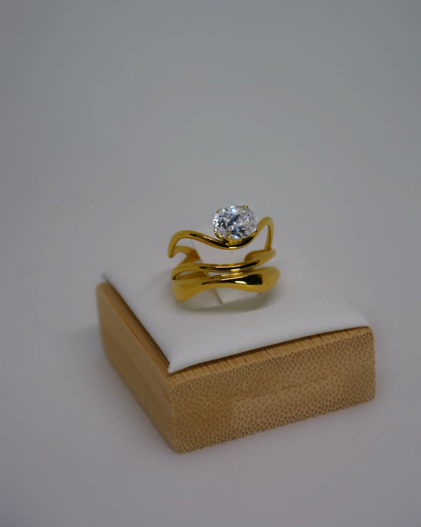 Ondine Ring 18K gold-plated abstract ring with wave-like curves and a cubic zirconia center stone, photographed on a soft neutral background in a refined, elegant style.