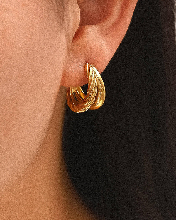 Aurum Twist Earrings, gold double-hoop earrings with braided and smooth textures, photographed on a neutral background with soft light for a refined luxury look.