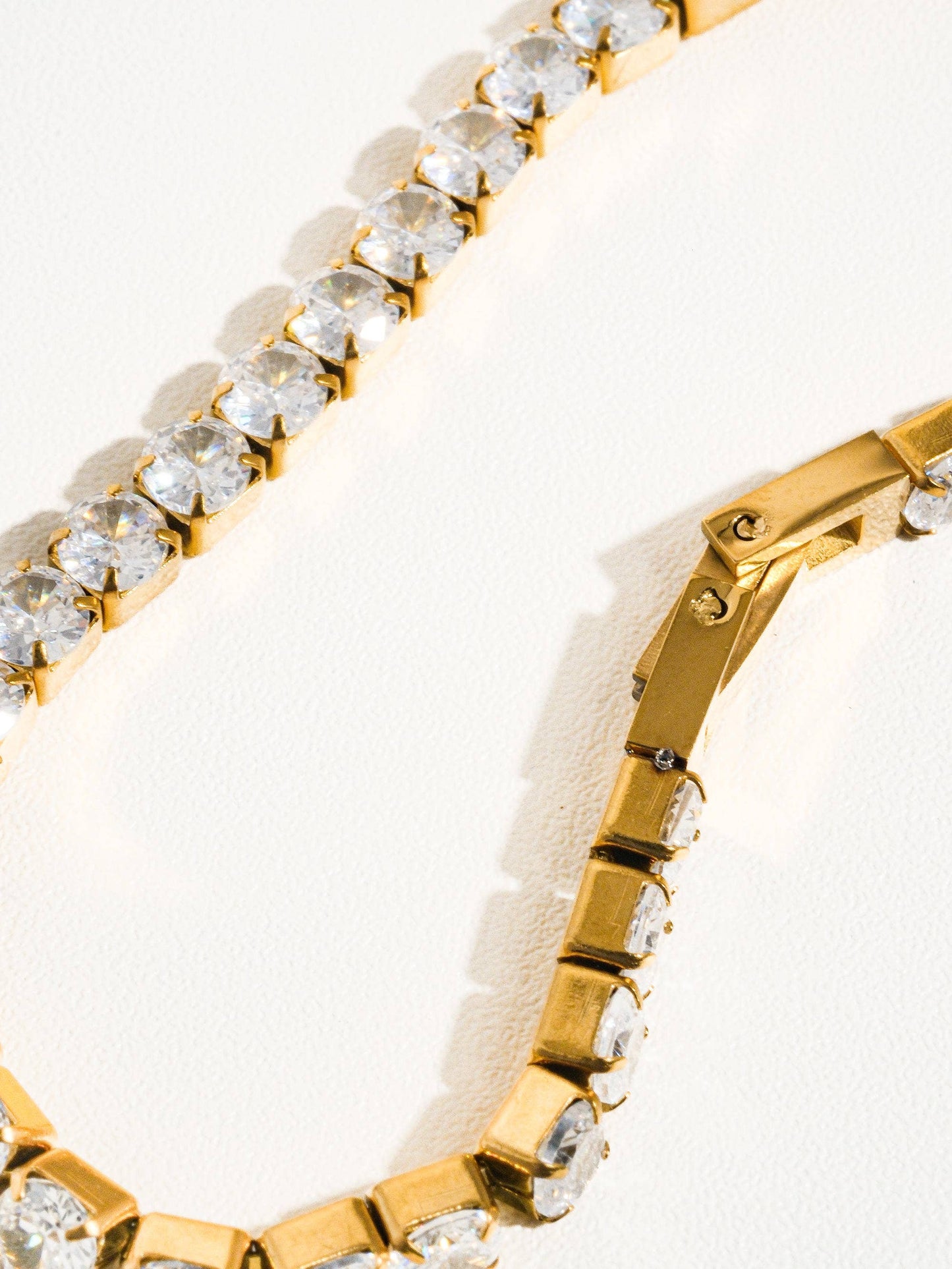 Lucente Bracelet, a gold stainless-steel tennis bracelet adorned with cubic zirconia stones, photographed on a soft neutral background, glowing under gentle light.
