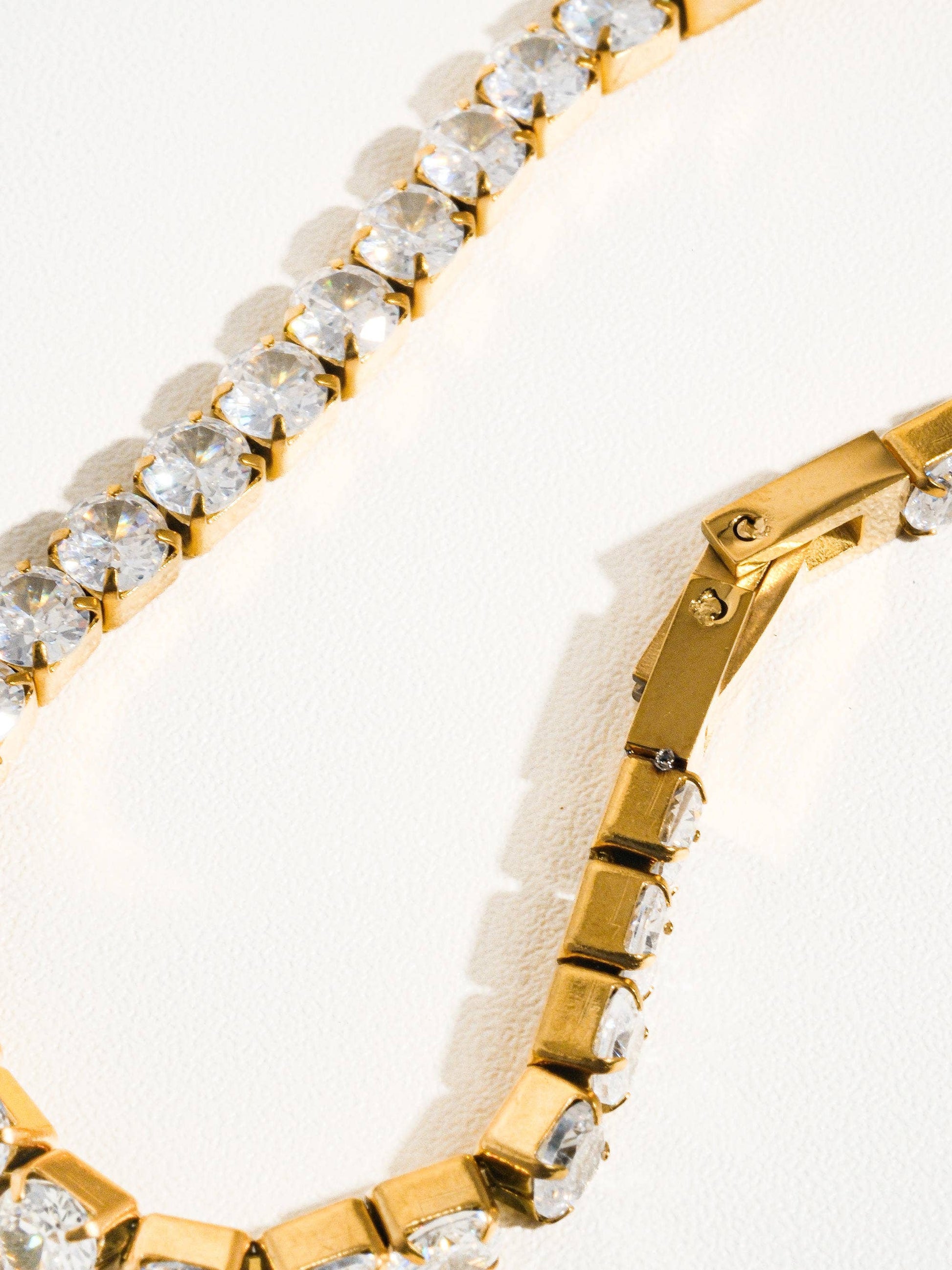 Lucente Bracelet, a gold stainless-steel tennis bracelet adorned with cubic zirconia stones, photographed on a soft neutral background, glowing under gentle light.