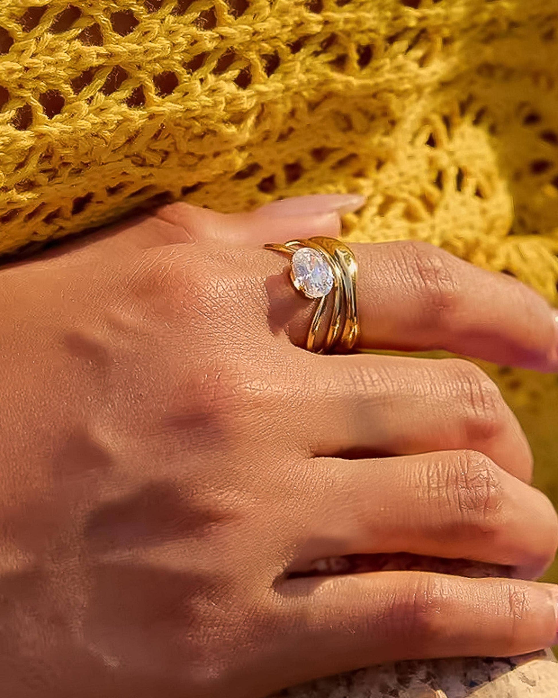 Ondine Ring 18K gold-plated abstract ring with wave-like curves and a cubic zirconia center stone, photographed on a soft neutral background in a refined, elegant style.