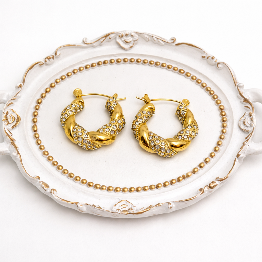 Gold twisted hoop earrings with clear zirconia stones on decorative tray by Atelier Épure — elegant, timeless, and refined.