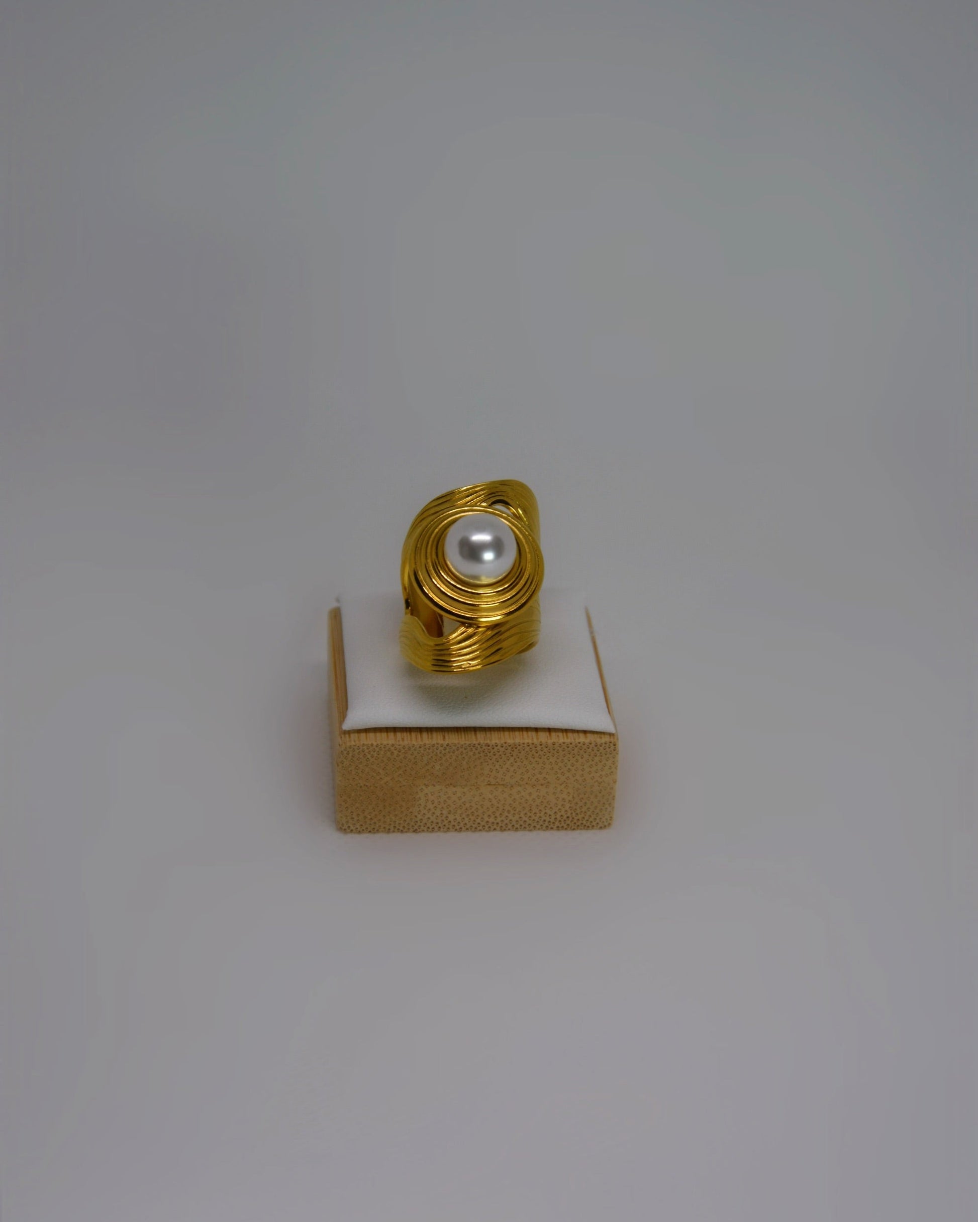 Cendréa Ring adjustable gold-tone stainless steel ring with wave texture and central pearl, photographed in soft neutral tones for a refined Atelier ÉPURE aesthetic.