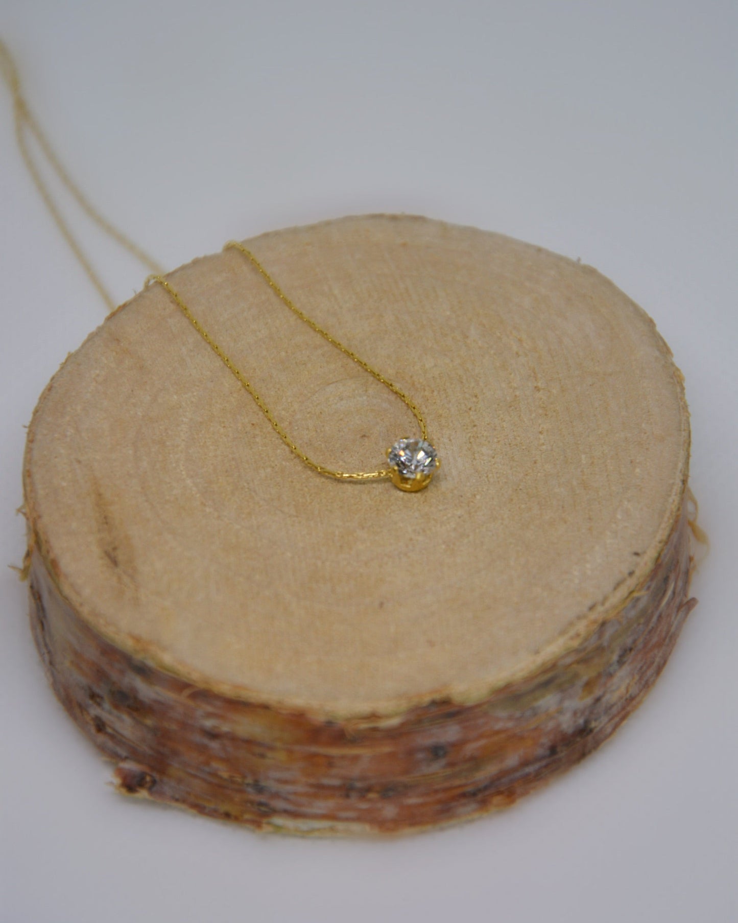 Close-up of the Serein Necklace, a dainty 18K gold-plated chain featuring a small round cubic zirconia pendant, photographed on a soft neutral display.