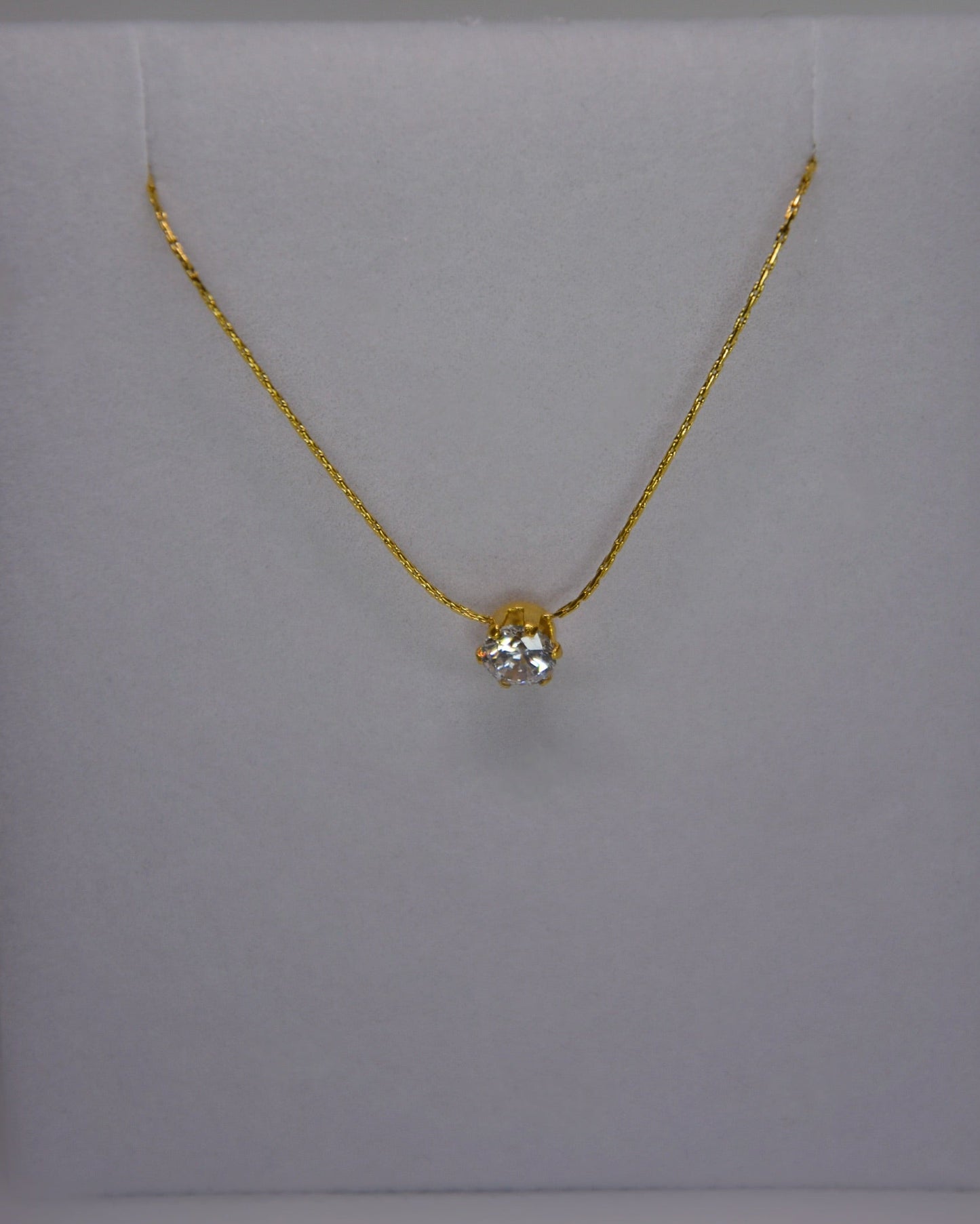 Close-up of the Serein Necklace, a dainty 18K gold-plated chain featuring a small round cubic zirconia pendant, photographed on a soft neutral display.