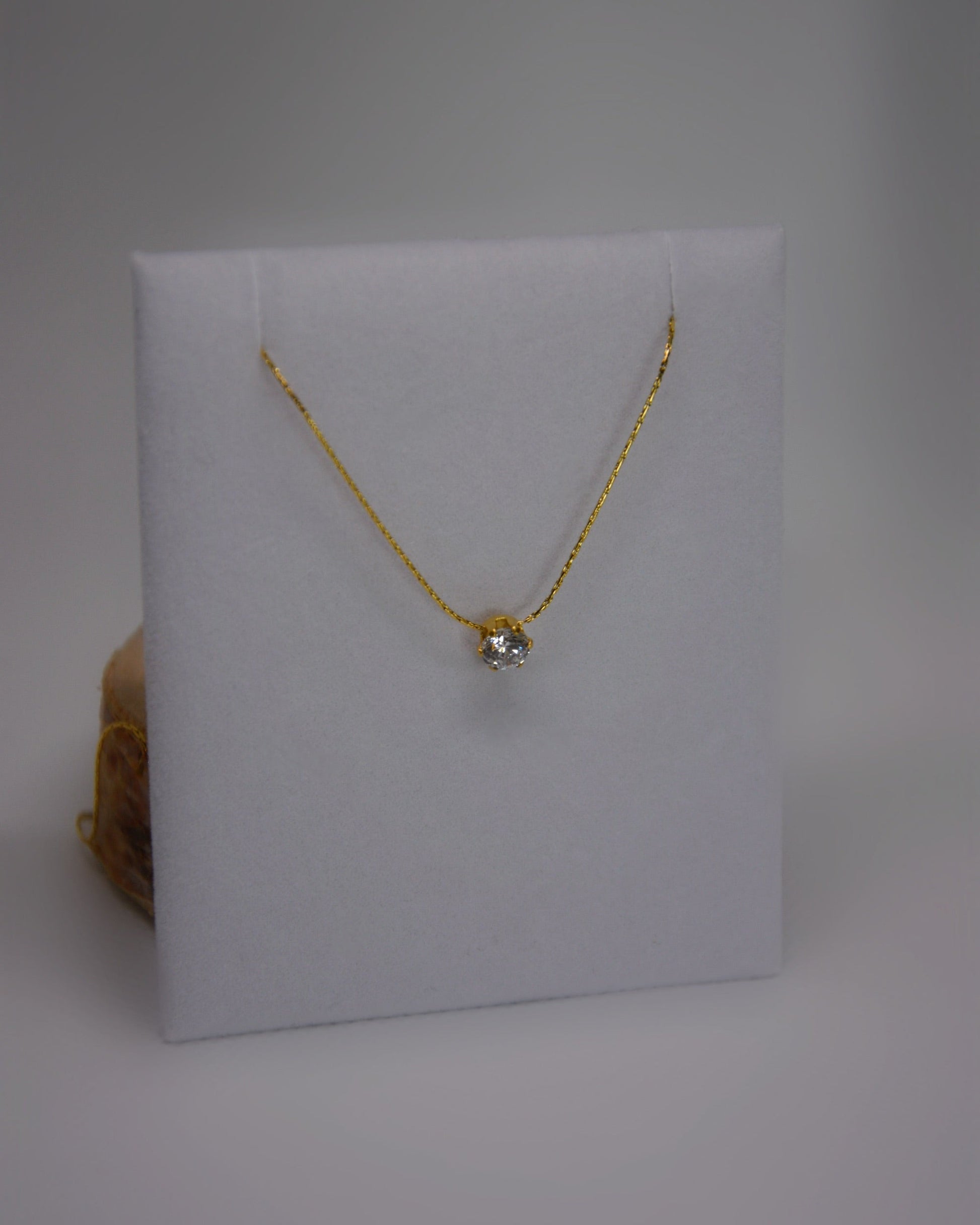Close-up of the Serein Necklace, a dainty 18K gold-plated chain featuring a small round cubic zirconia pendant, photographed on a soft neutral display.
