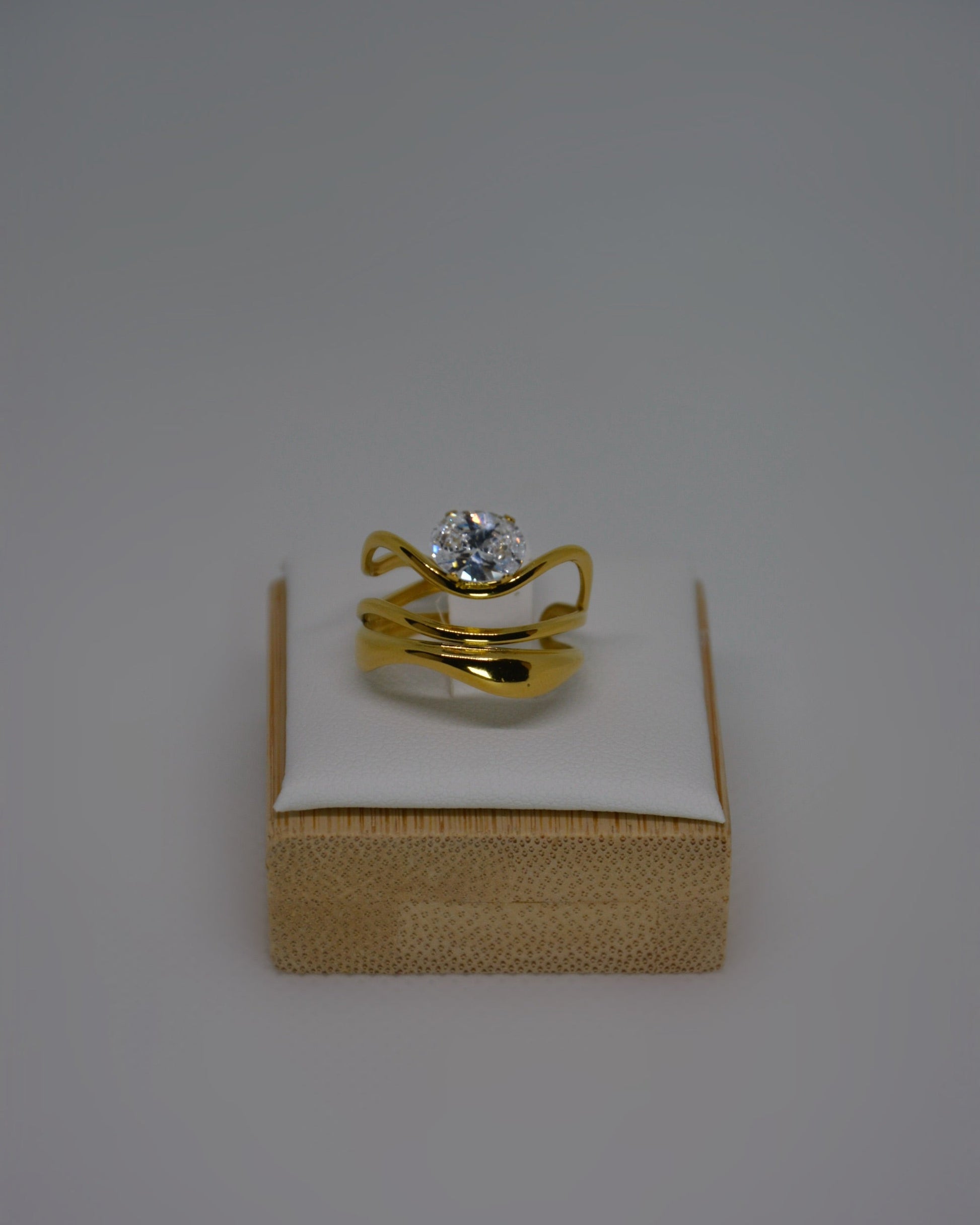 Ondine Ring 18K gold-plated abstract ring with wave-like curves and a cubic zirconia center stone, photographed on a soft neutral background in a refined, elegant style.