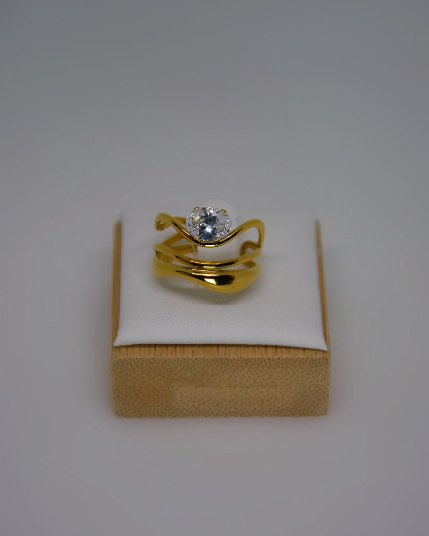 Ondine Ring 18K gold-plated abstract ring with wave-like curves and a cubic zirconia center stone, photographed on a soft neutral background in a refined, elegant style.