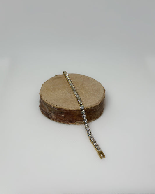 Lucente Bracelet, a gold stainless-steel tennis bracelet adorned with cubic zirconia stones, photographed on a soft neutral background, glowing under gentle light.