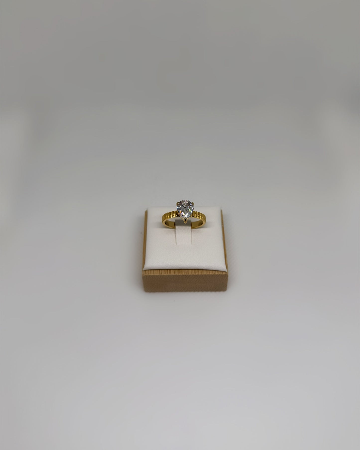 Close-up of the Vow Ring an 18K gold-plated stainless-steel statement ring featuring a pear-cut cubic zirconia, photographed on a soft neutral display.