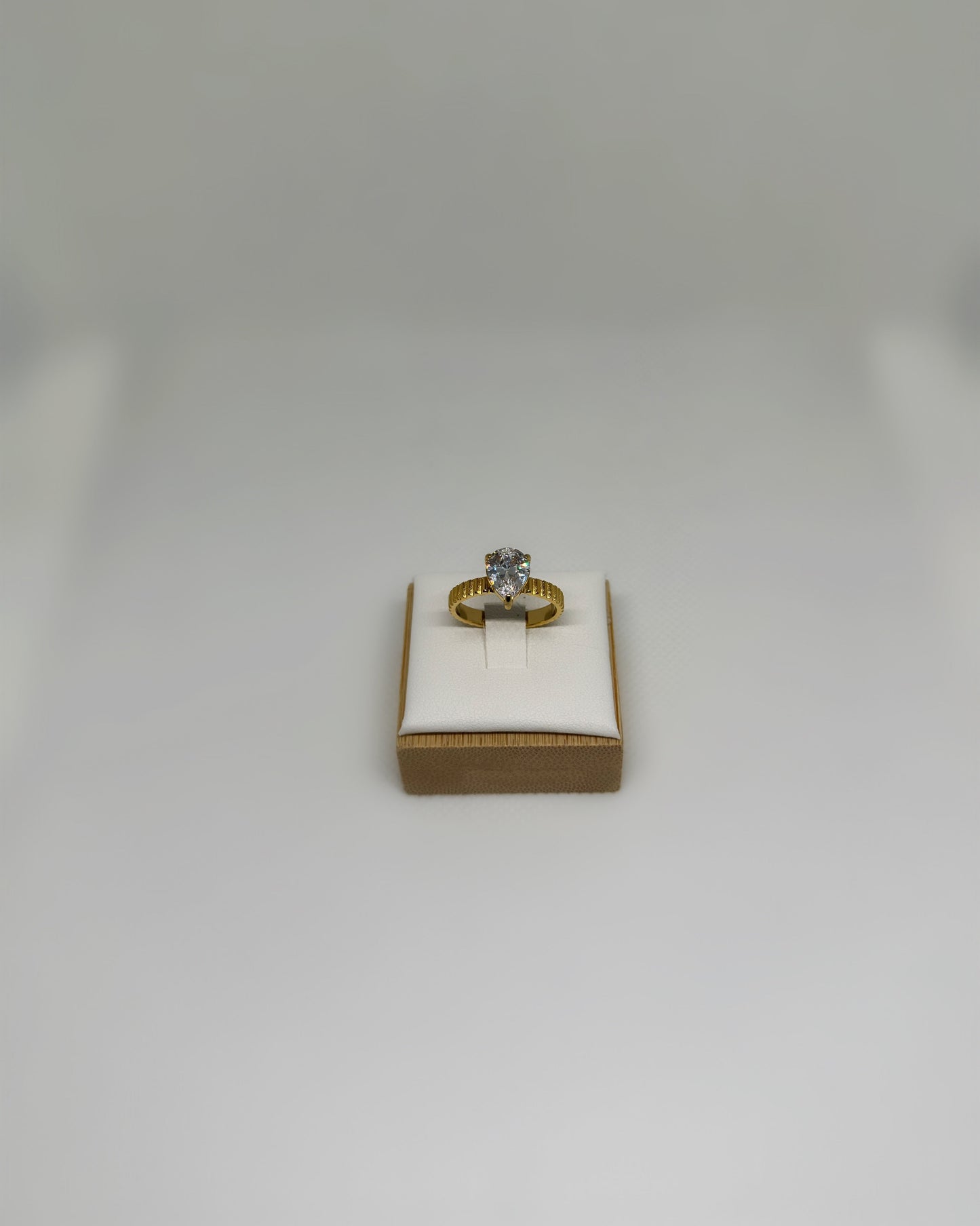 Close-up of the Vow Ring an 18K gold-plated stainless-steel statement ring featuring a pear-cut cubic zirconia, photographed on a soft neutral display.