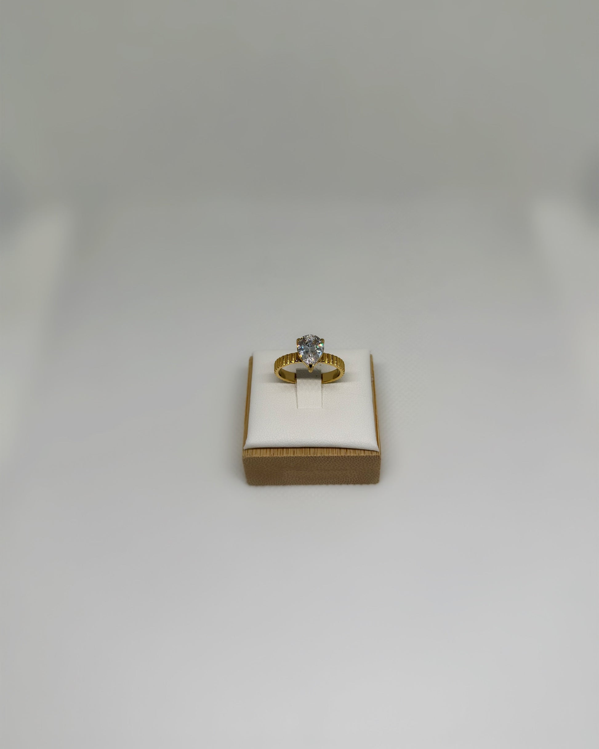 Close-up of the Vow Ring an 18K gold-plated stainless-steel statement ring featuring a pear-cut cubic zirconia, photographed on a soft neutral display.