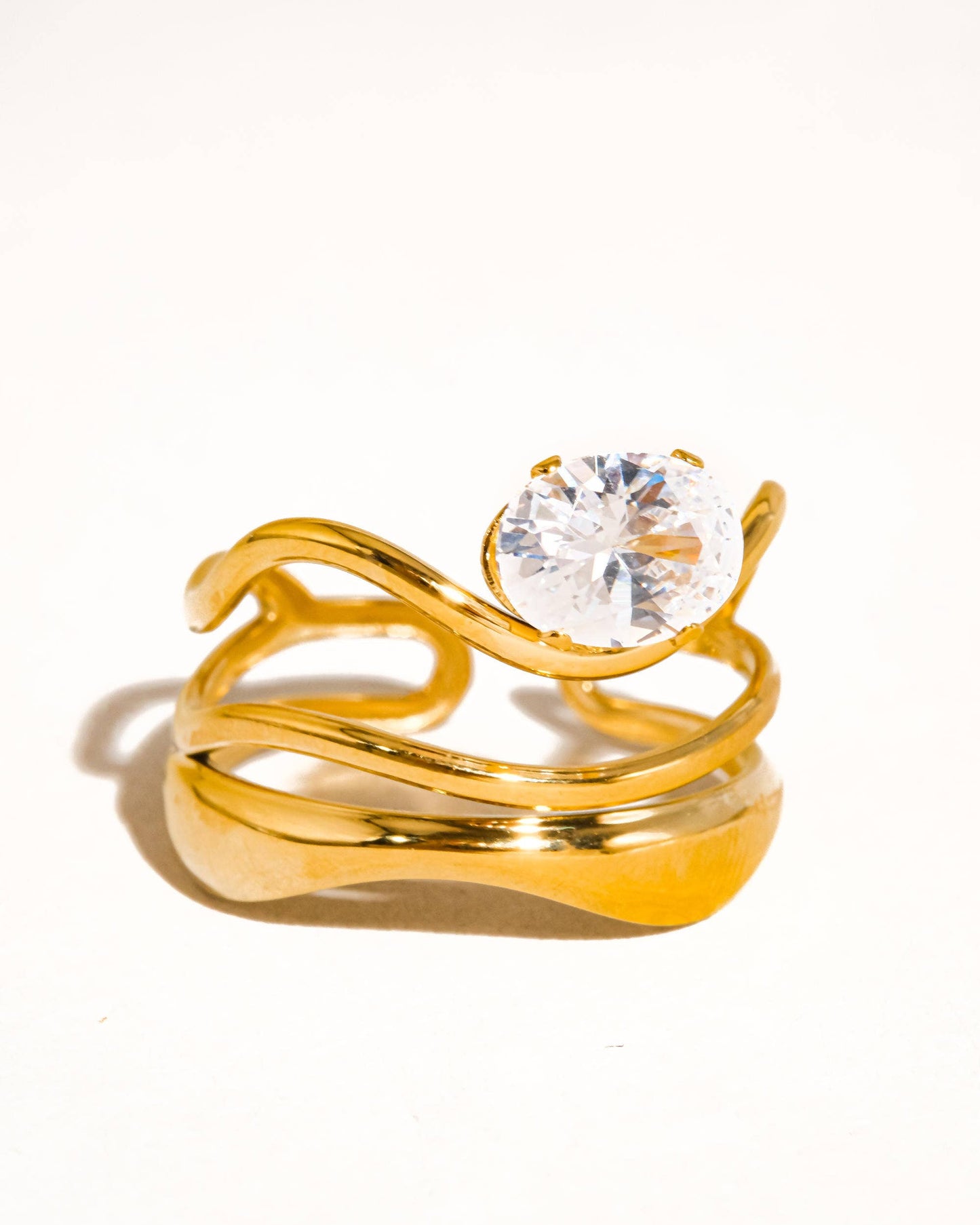 Ondine Ring 18K gold-plated abstract ring with wave-like curves and a cubic zirconia center stone, photographed on a soft neutral background in a refined, elegant style.