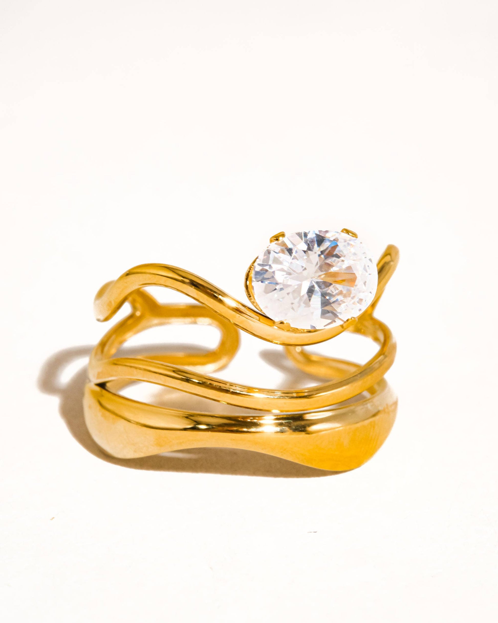 Ondine Ring 18K gold-plated abstract ring with wave-like curves and a cubic zirconia center stone, photographed on a soft neutral background in a refined, elegant style.